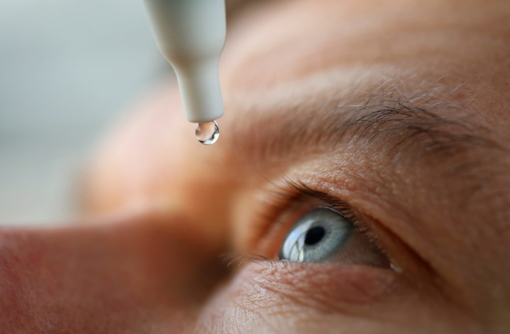 A close-up view of a man with blue eyes putting in eye drops