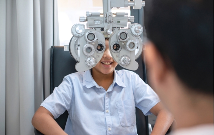 A young boy at his optometrists looking through an optical phoropter during his regular eye exam