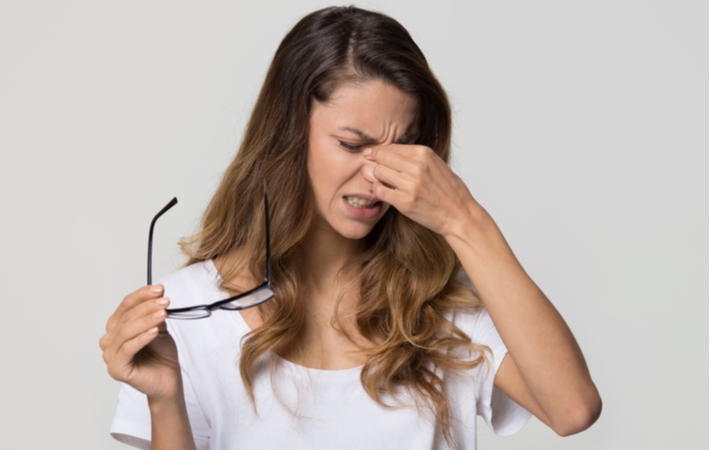 A woman holding her glasses while rubbing her eyes with a look of frustration as she suffers from dry eye