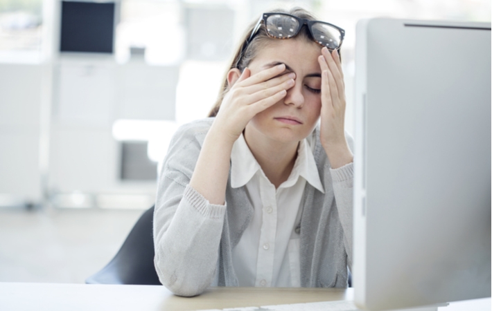 A woman using a desktop computer rubbing her eye's that feel sore and fatigued
