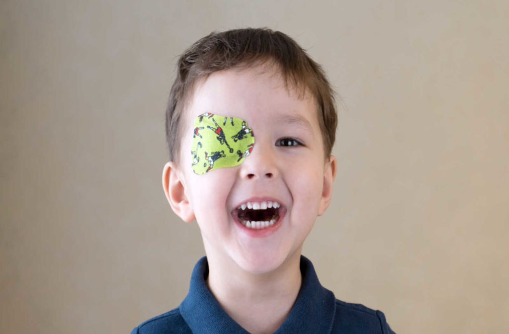 A young boy wearing a green eye patch to treat lazy eye smiles with his mouth open.