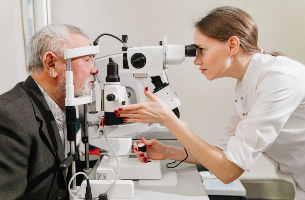 A senior man is receiving an eye exam from a female optometrist, who is using a specialized machine to examine his eyes.