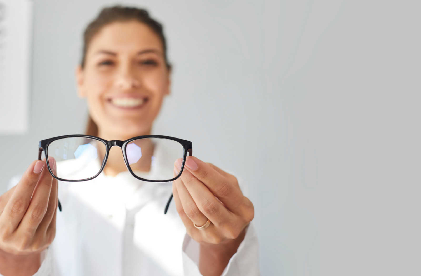 An optometrist smiling and holding a prescription eyeglass