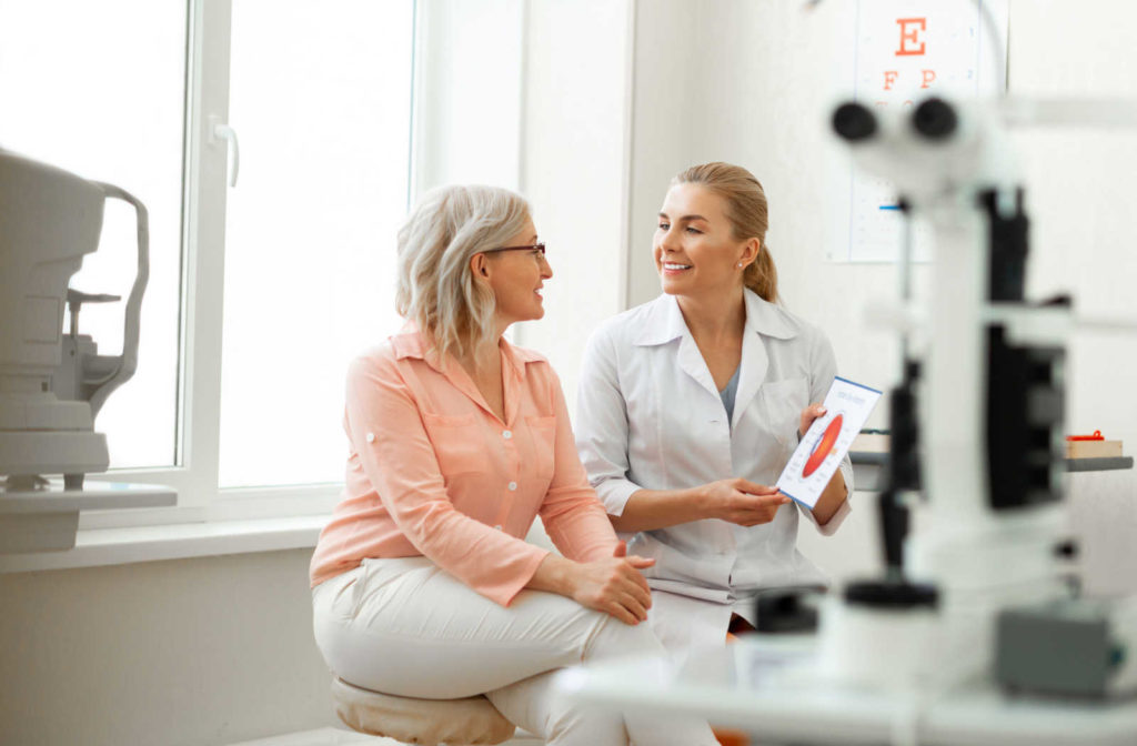 A senior woman sitting in an optometrist's office, smiling and talking to her eye doctor