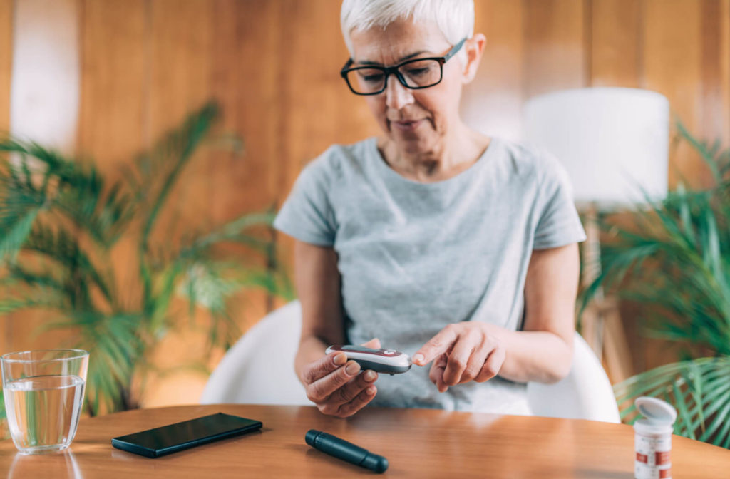 A senior woman in a brightly lit room using a glucometer to monitor her blood sugar levels.