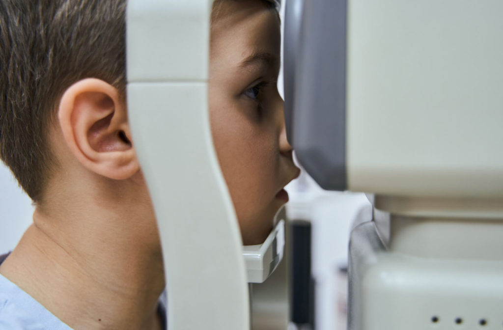 A boy is looking through a refractometer to determine the correct eyeglass or contact lens prescription.