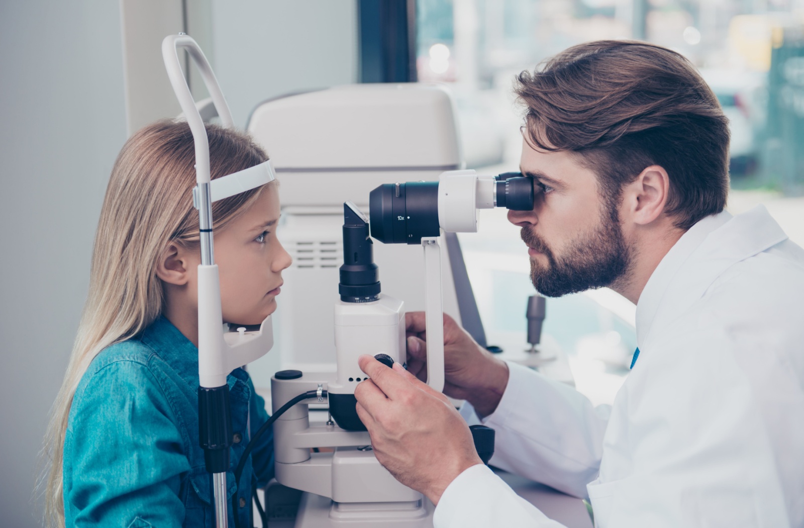 A male optometrist using a medical device to examine the eyes of a young child and look for potential eye problems.
