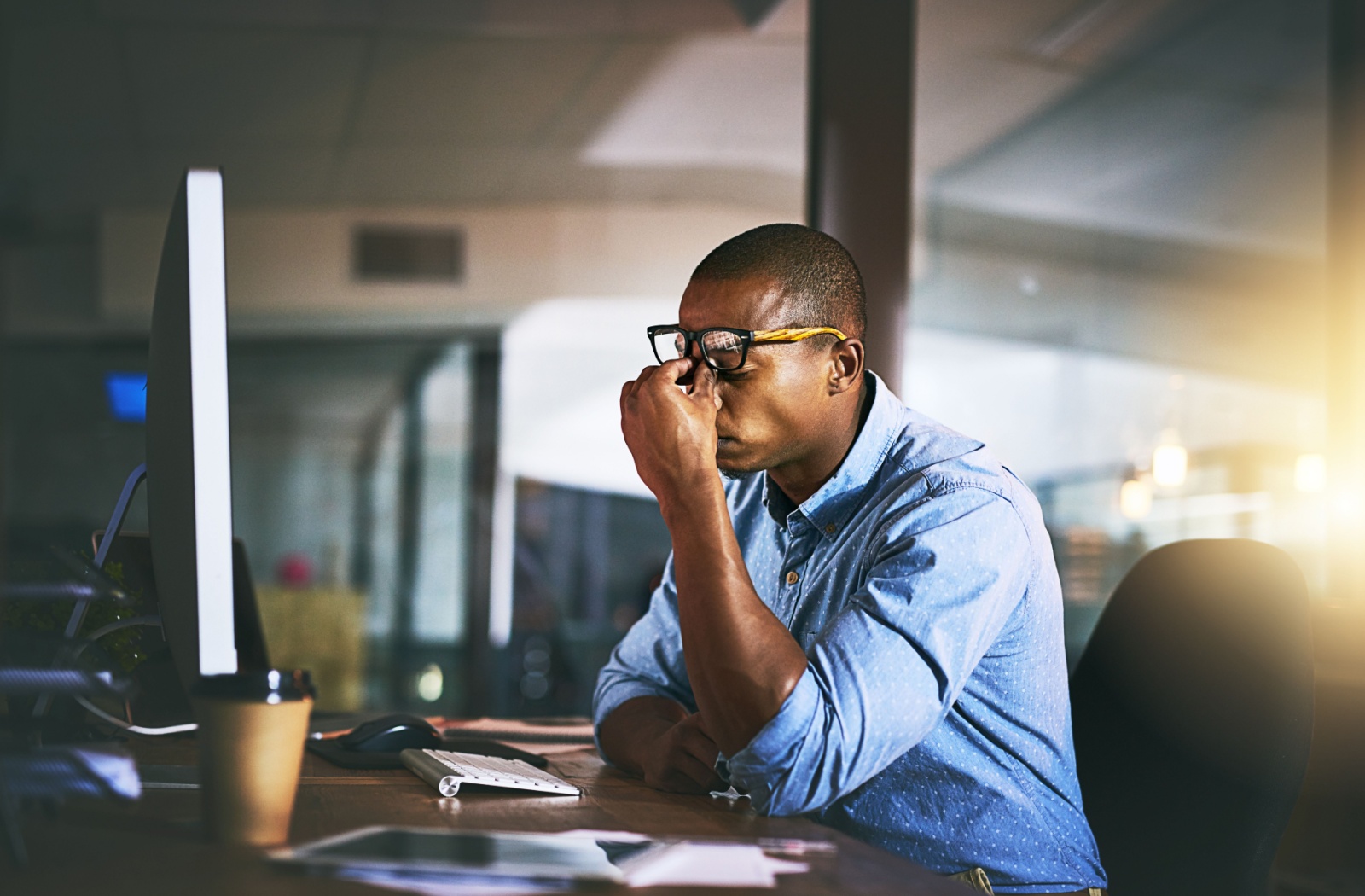 A stressed man at work rubs his eyes, potentially spreading bacteria from his hands