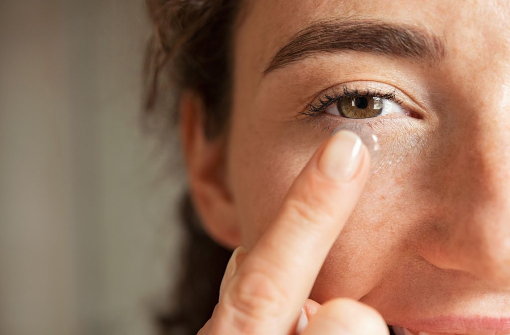 A close-up image of a woman carefully putting a contact lens into her right eye.