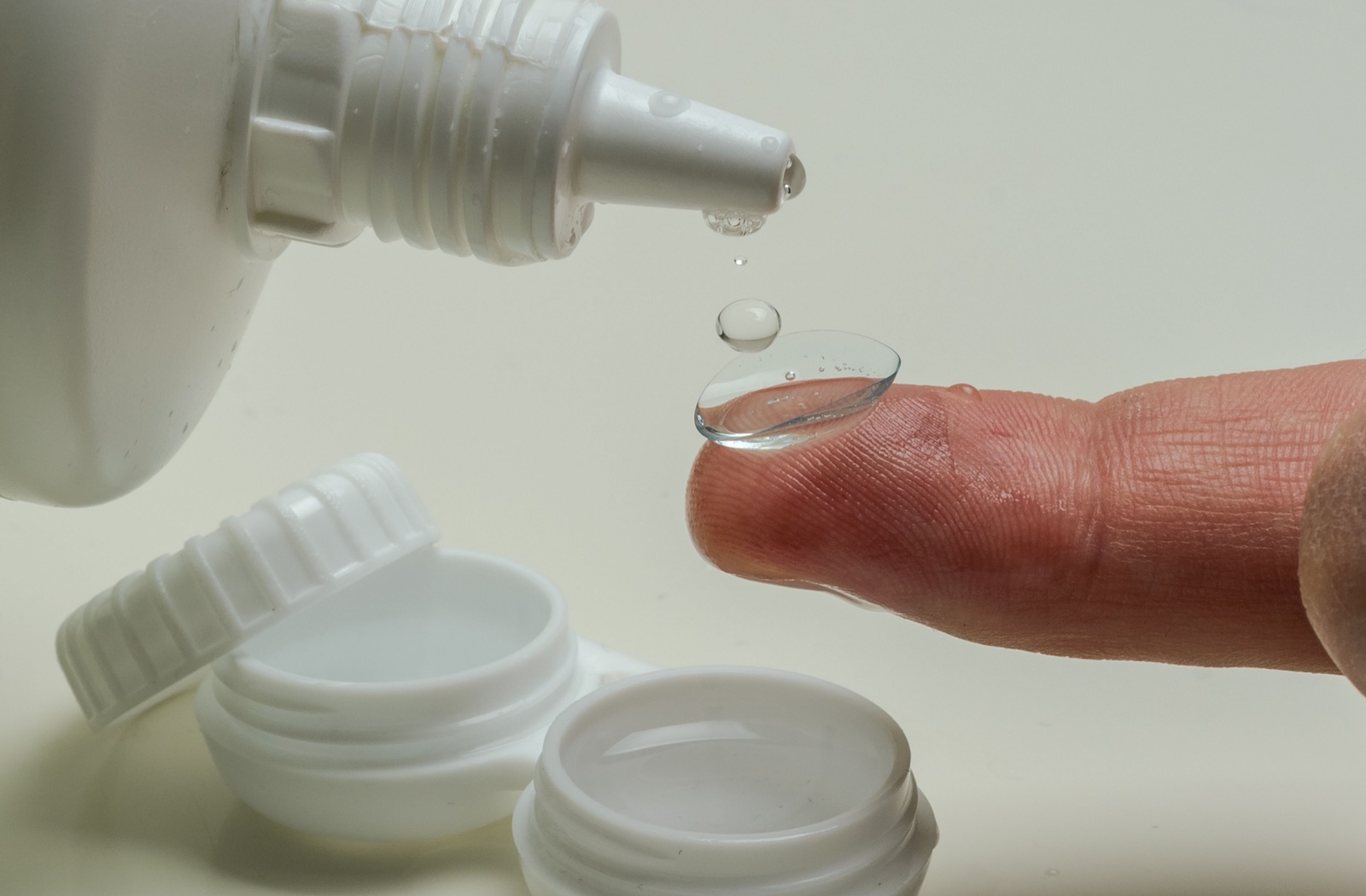 A close-up image of a person cleaning a contact lens on the tip of their finger.
