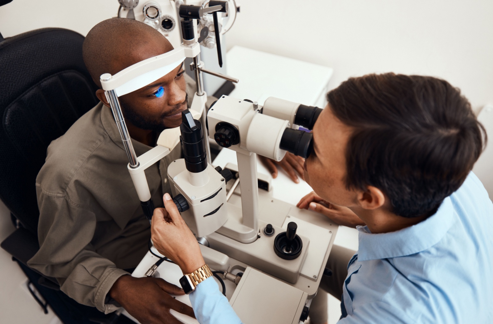 A patient sits in front of a slit lamp while an optometrist looks through it to examine the patient's eye.