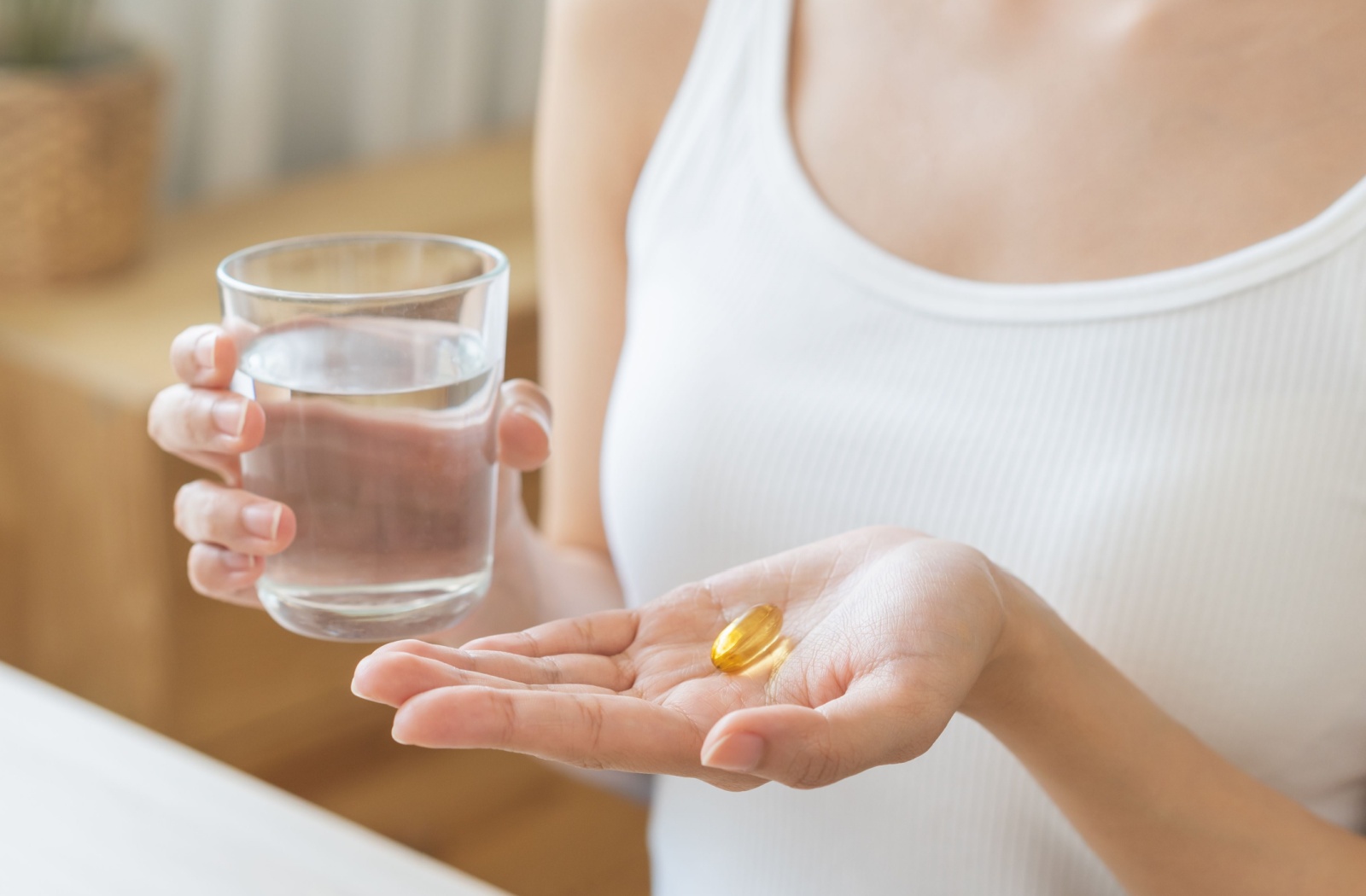 A close up of a woman holding a glass of water in one hand and an omega 3 pill in the other.