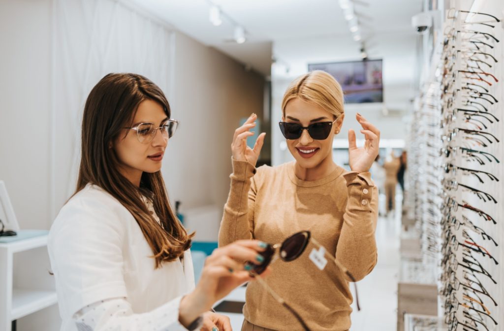 An optometrist helping a patient choose between polarized and non-polarized lenses in front of a wall of sunglasses.