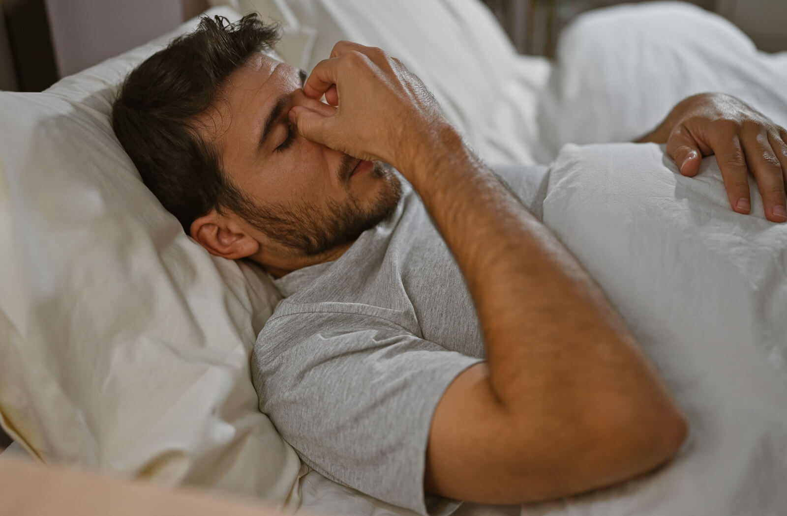 A young adult rubbing the bridge of their nose in discomfort due to waking up with dry eyes.
