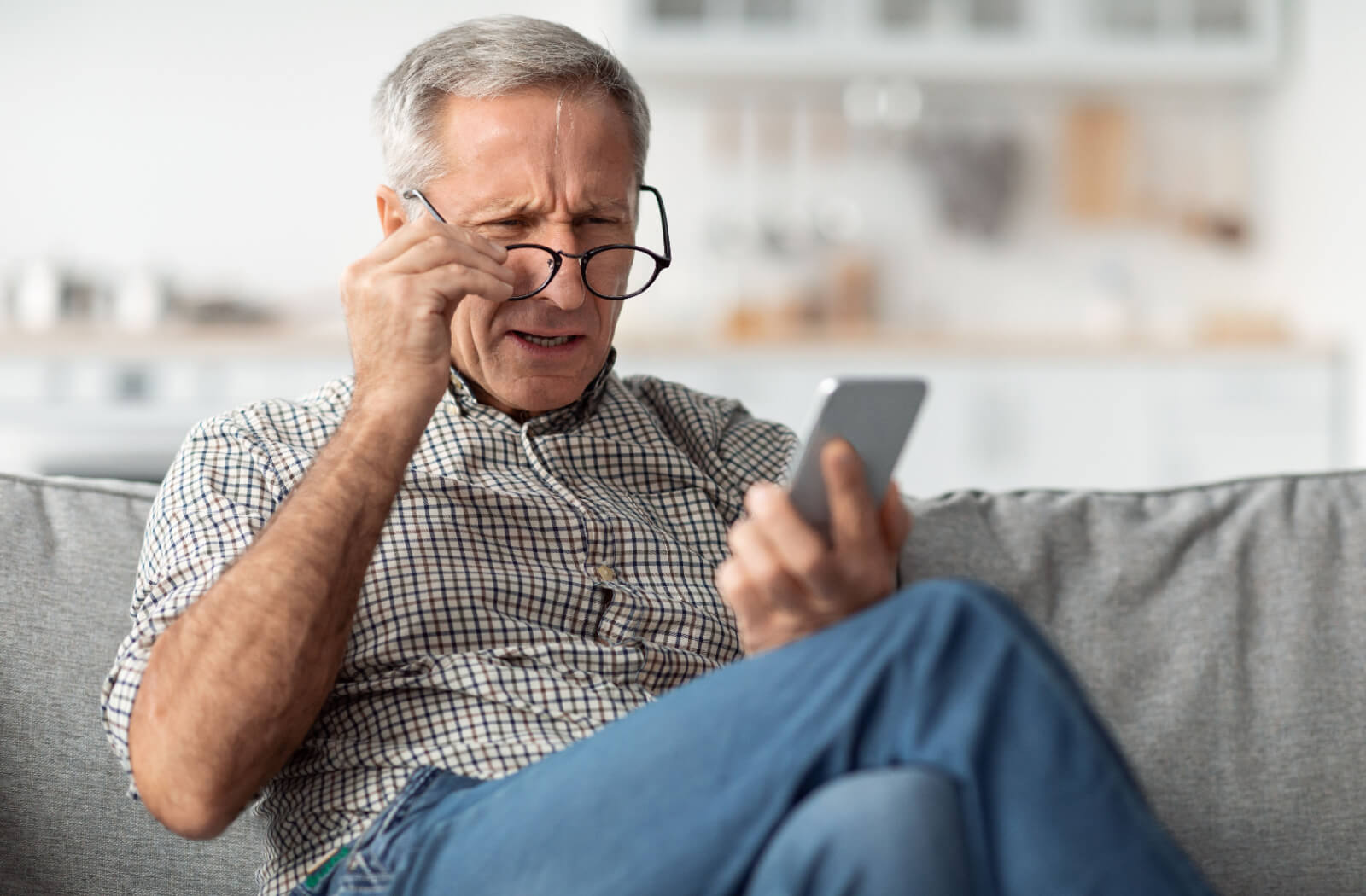 An older adult adjusting their glasses in frustration while trying to read their phone due to vision problems from cataracts.
