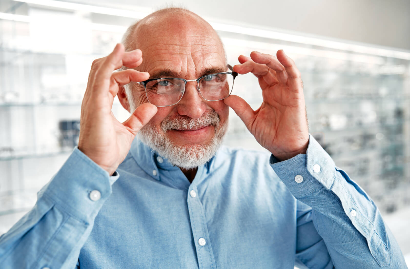 An older adult smiling while adjusting their new glasses after an eye exam in an optometry office.
