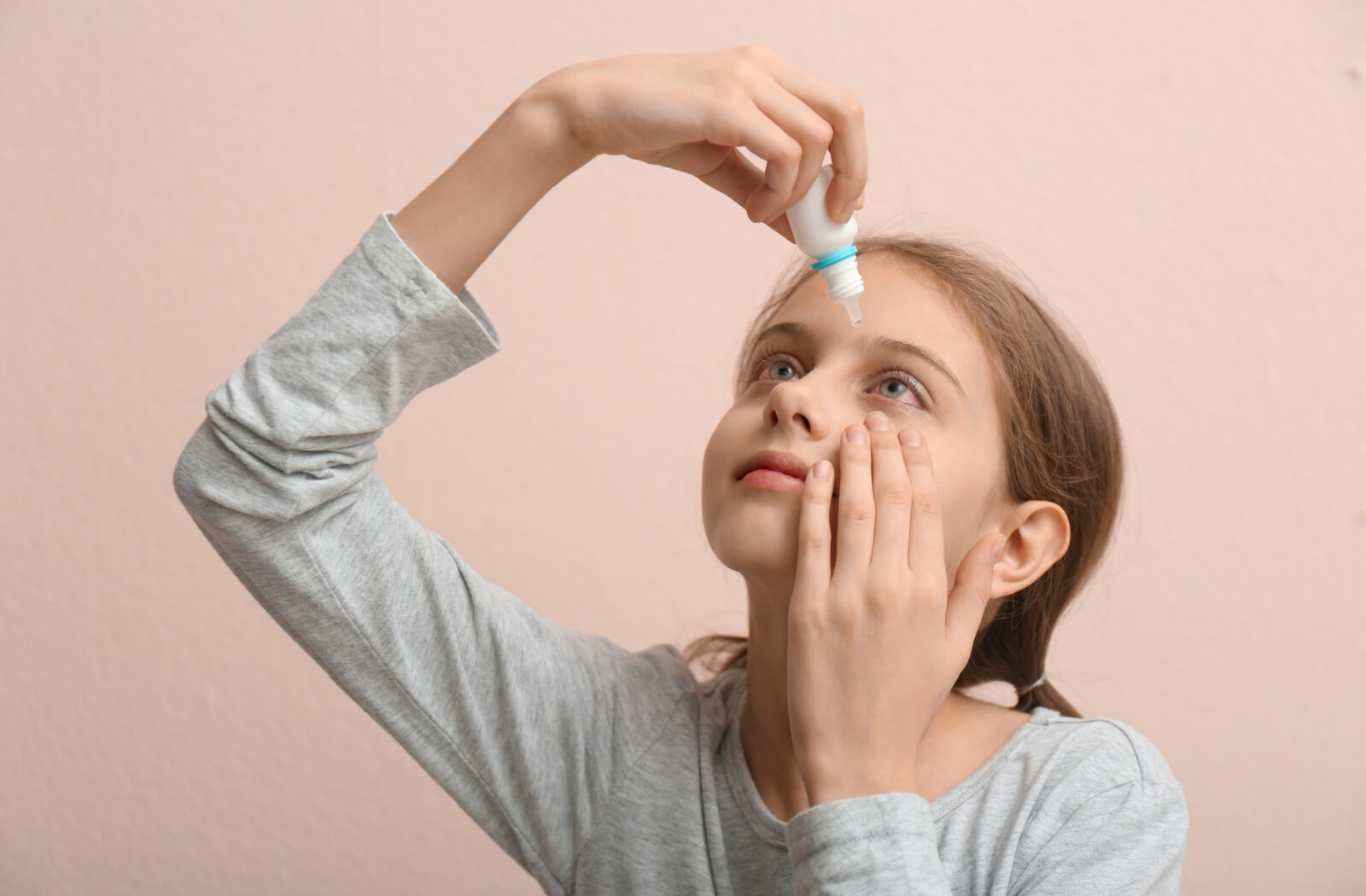 A child with pink eye carefully applying eye drops to their left eye.
