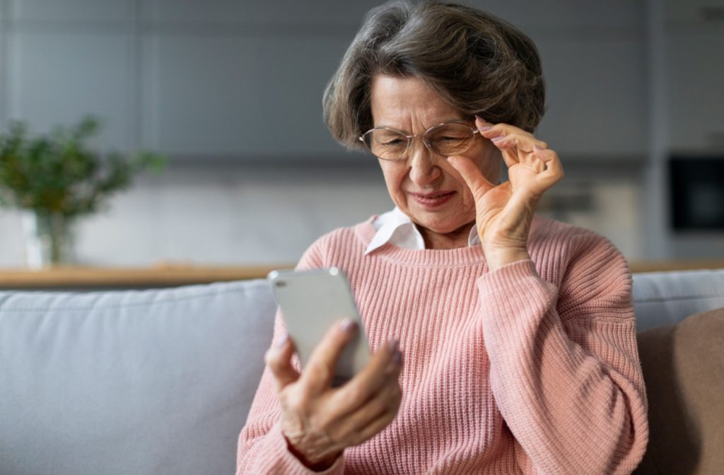 An older adult lowering their glasses while looking at their phone due to vision problems from cataracts.