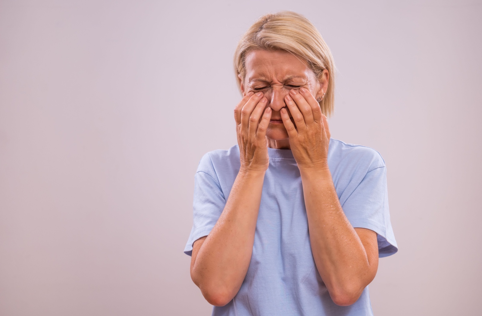 Woman in discomfort pressing her hands against her cheeks showing sinus pressure and facial pain symptoms