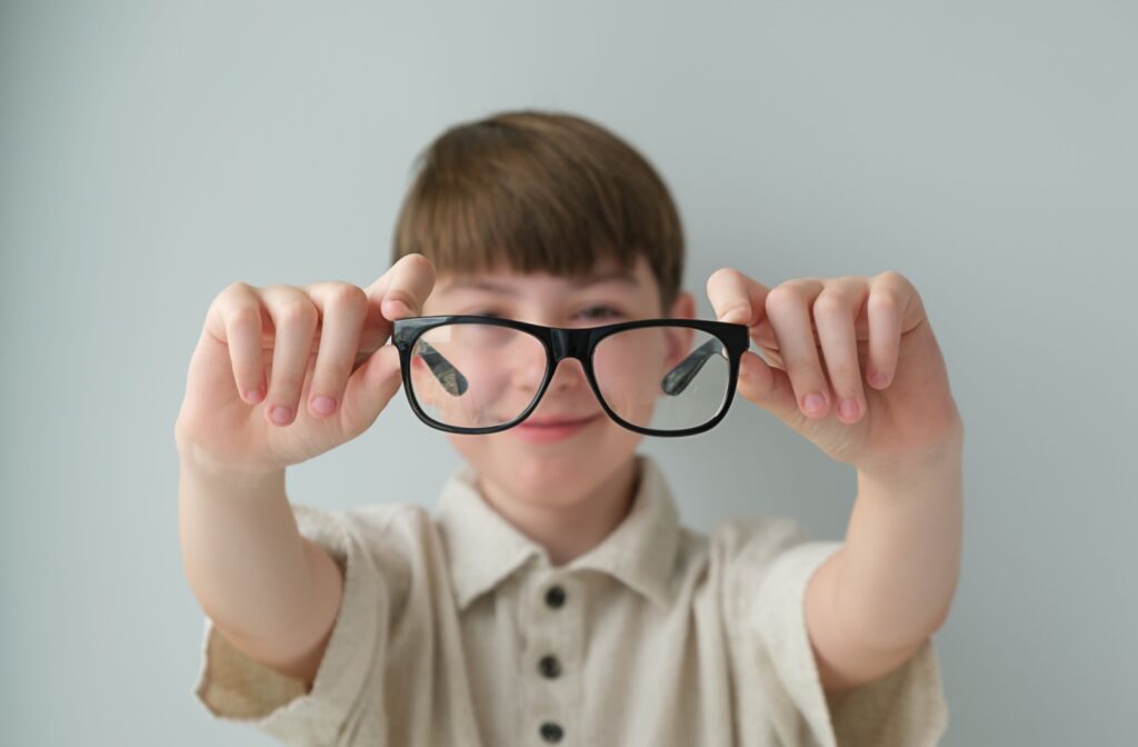 Closeup with a child holding up glasses to their face, with them blurred in the background.