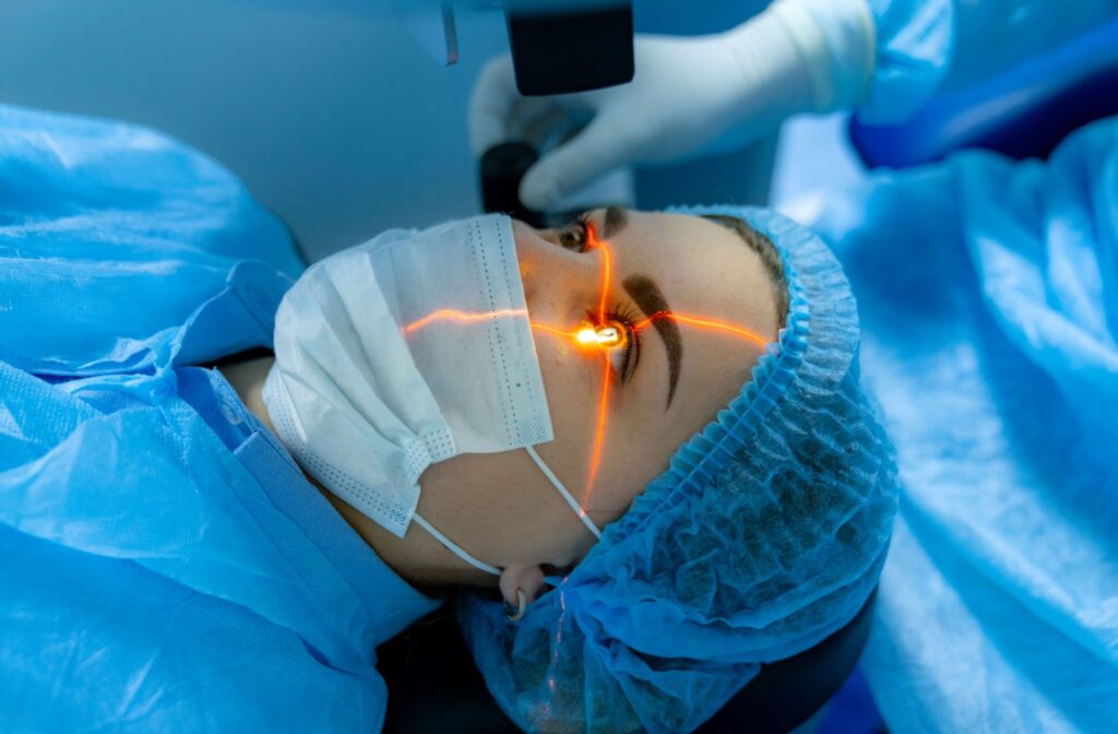 Patient undergoing laser eye surgery with protective coverings and a visible red laser targeting the eye, guided by a medical professional in surgical attire.