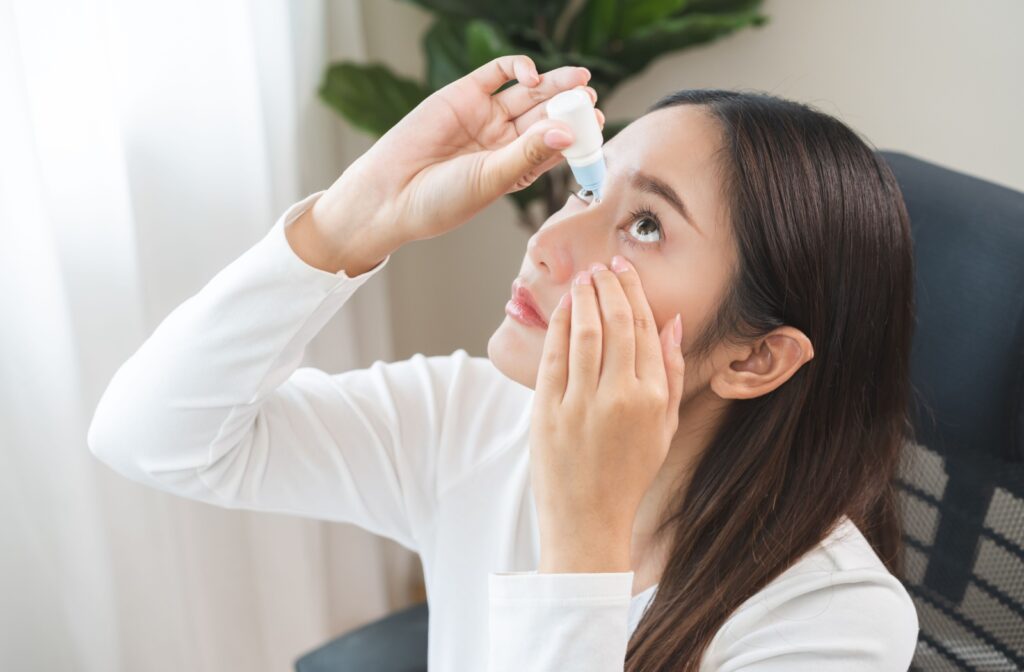 Woman applying lubricating eye drops while sitting indoors, supporting a smooth recovery after an eye procedure like laser vision correction.