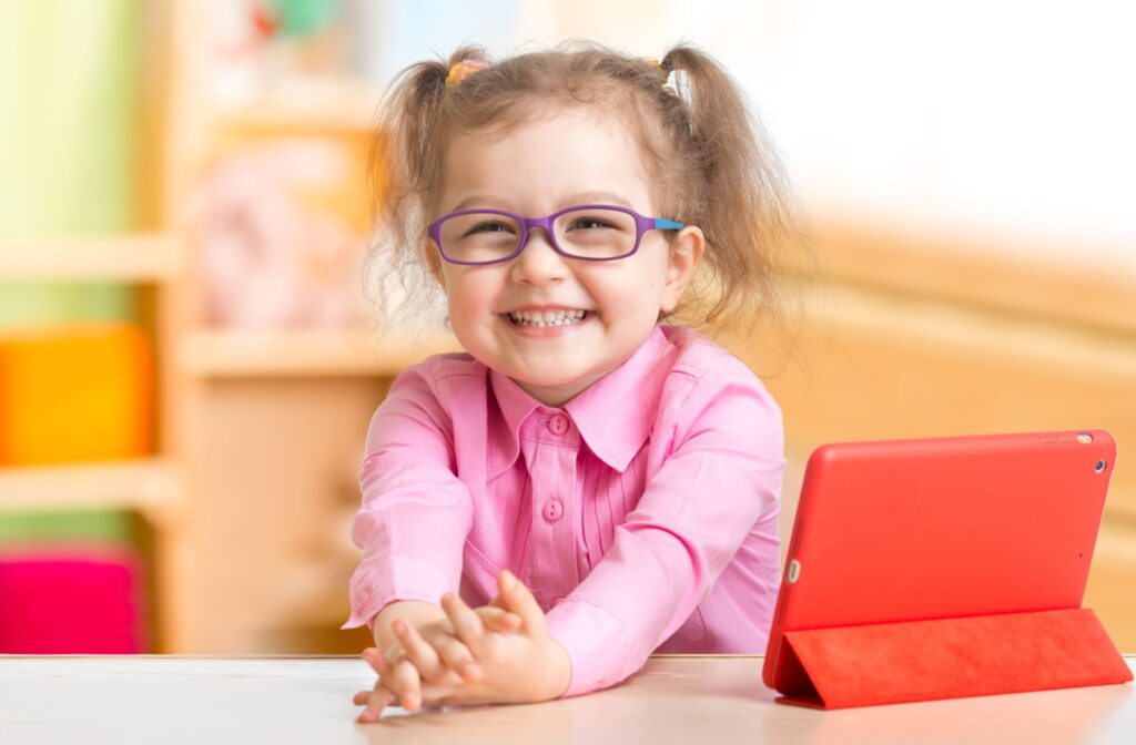 Young girl with glasses sitting smiling in a classroom. 