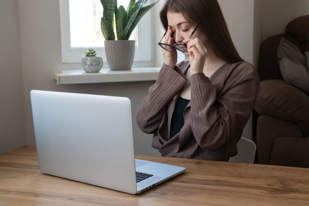 Girl working on a computer holding her right eye from eye strain.